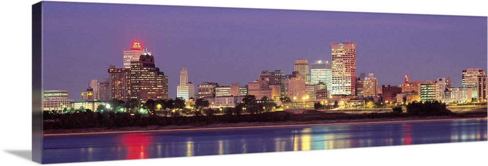 Panoramic photograph of skyline with buildings lit up and reflecting off the waterfront at night.