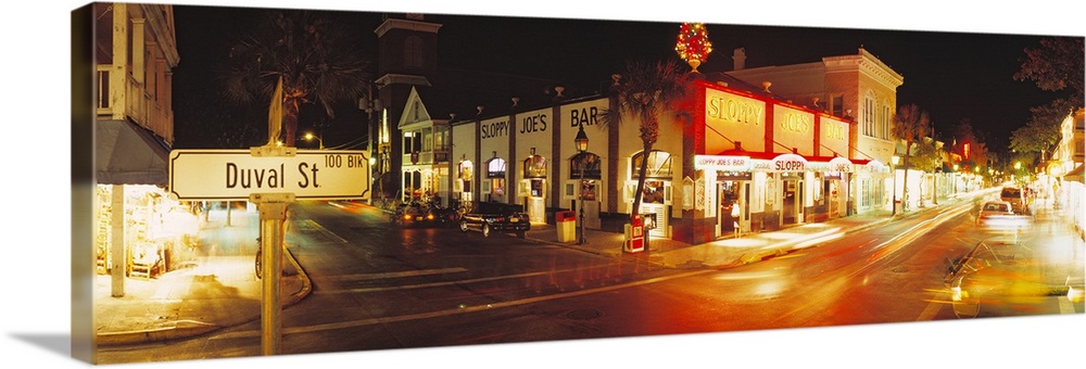 Panoramic photograph taken of a street in Key West during the night with the shops lit up on the sides.