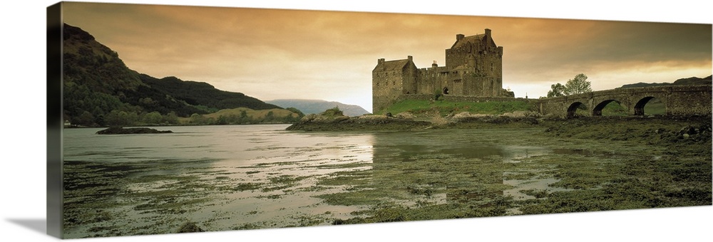 Wide angle photograph taken of a castle in Scotland under a dusk sky with wet land shown in the foreground and hills shown...