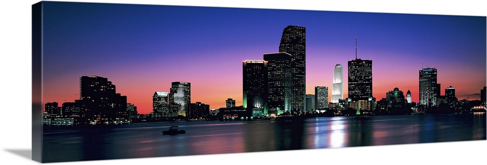 Giant, panoramic photograph of the Miami skyline at night, reflecting over the waters of Biscayne Bay.