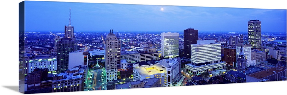 This panoramic wall art is an aerial photograph of the city skyline at dusk with moon shining down on the city.