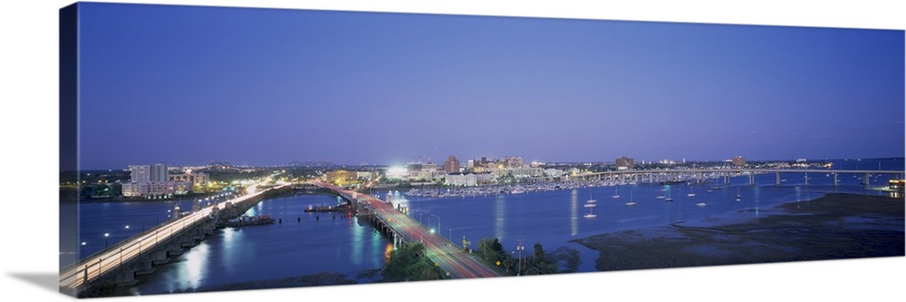 Panoramic photograph on a big canvas of two bridges over water, leading toward the brightly lit Charleston skyline at night.