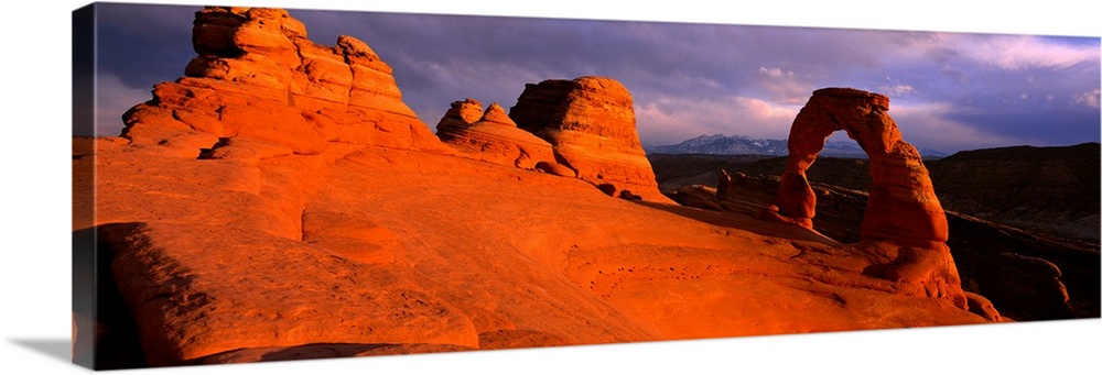 A landscape photograph that is a panoramic shot of a wind eroded rock face illuminated a sunset.