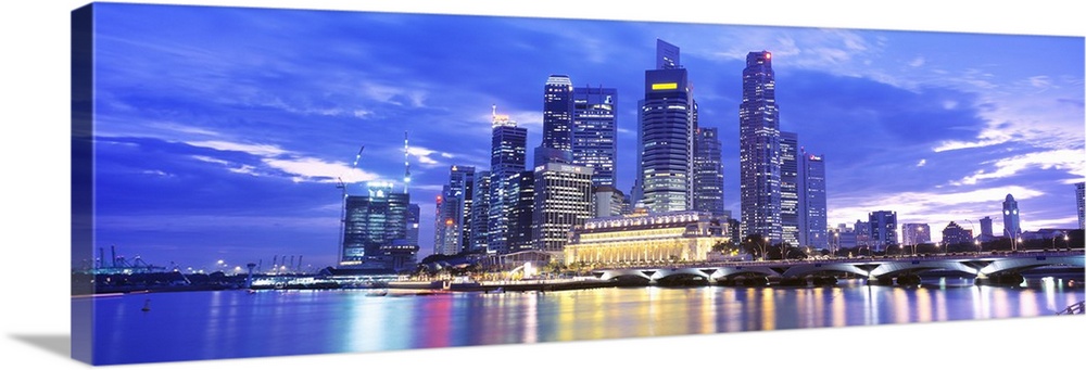 A large panoramic photograph taken of a skyline in Singapore during the evening with all of the buildings lit up and refle...
