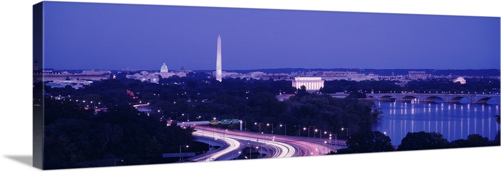 Wide angle view of the nations capital during dusk with the monuments lit up and the highway illuminated with cars lights.
