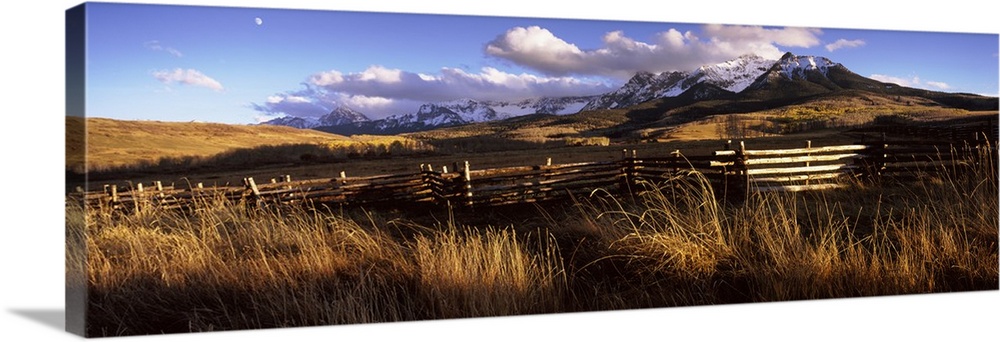 A large panoramic picture of Colorado mountains with a fence and tall grass in the foreground.