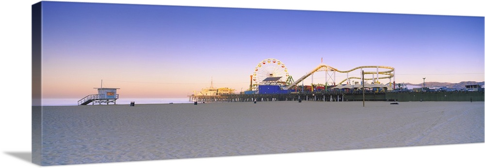 This is a panoramic photograph of a board walk carnival taken from a sandy beach at twilight.