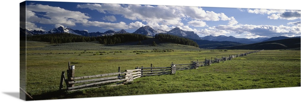 Panoramic picture taken of a vast field with a small wooden fence going as far back as you can see. Mountains line the bac...