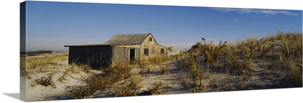A shack sits on the beach just behind the dunes that are covered with grass.