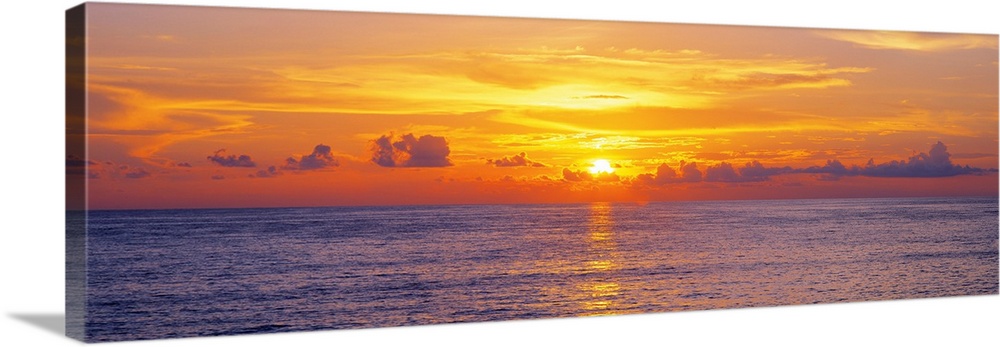 This panoramic seascape shows the sun setting behind clouds on the horizon in this photographic art for the home or office.