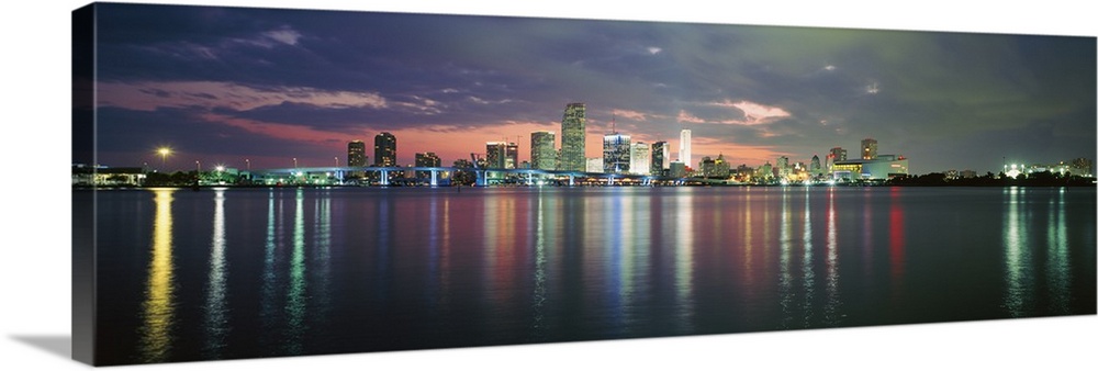 This city scape photograph shows the city from a distance reflecting on the water on panoramic shaped wall art.