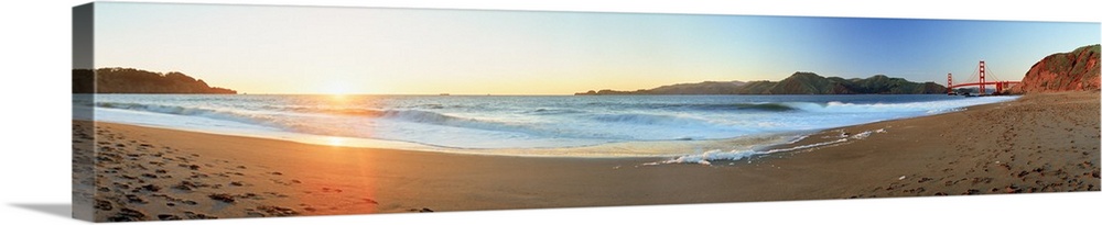 Long panoramic photo of a beach with the golden gate bride on the far right and the setting sun on the far left.