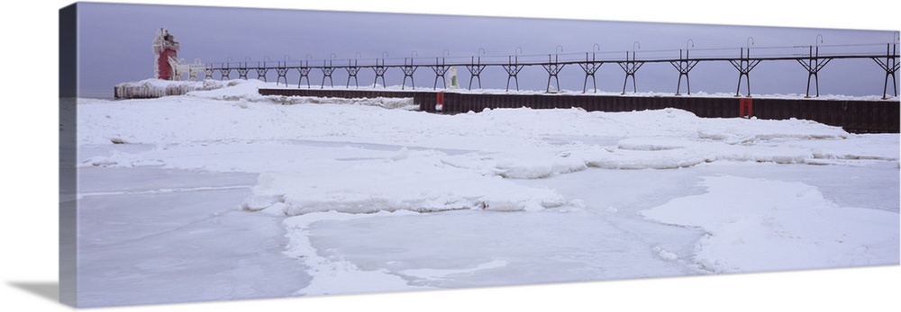Panoramic photograph of pier stretching into ice covered river leading to a tower with a guiding light at the top.