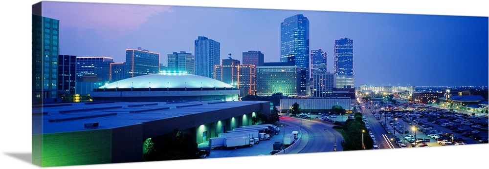 The city of Fort Worth is illuminated under a dusk sky with the buildings mostly shown to the left of this panoramic piece.