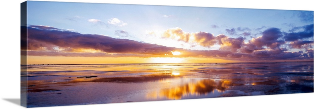 The sun breaks over the clouds in the horizon in this large panoramic photo from a beach on the North Sea in Germany.
