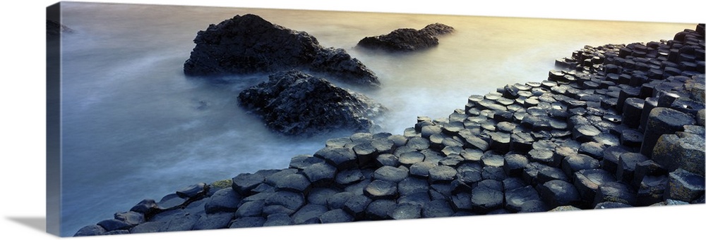 Panoramic photograph of rocky shoreline with large stone formations rising from mist covered ocean.