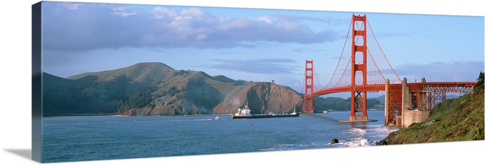 Wide angle photograph of the San Francisco Bay and the Golden Gate Bridge, mountains on the horizon, beneath a blue sky.