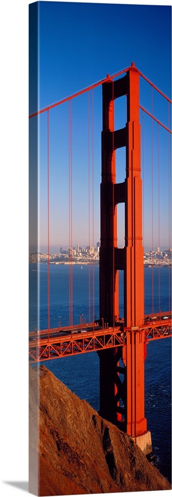 Tall panoramic photo of on of the main portions of the Golden Gate Bridge with cars driving across it and the cityscape in...
