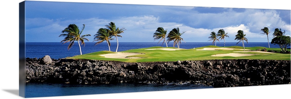 Panoramic photograph of golf course on a rock cliff stretching into the ocean on a cloudy day.  There are palm trees and s...