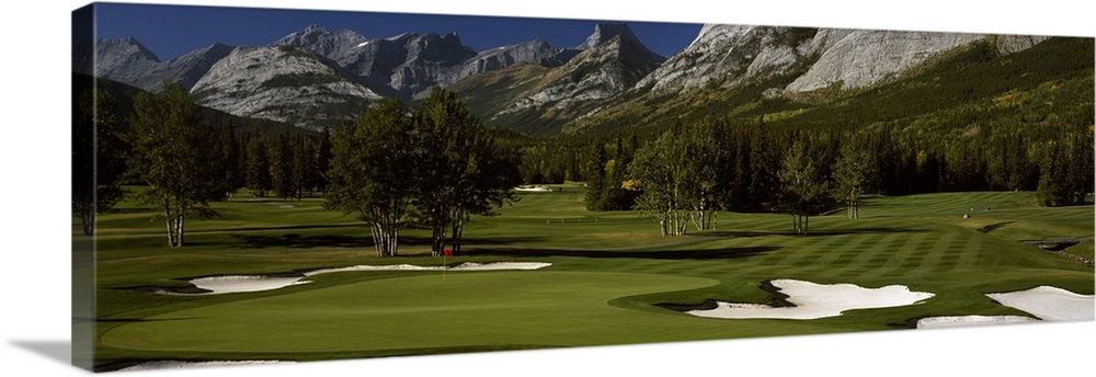 Panoramic photograph taken on a golf course of one of the holes that is surrounded by a mountain view.