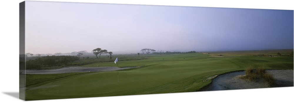 Giant landscape photograph of a flag surrounded by the rolling greens on Ocean Golf Course, beneath a hazy blue sky on Kia...