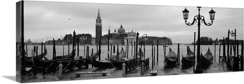 Wide angle photograph of a line of gondolas parked near the shore, the Church Of San Giorgio Maggiore on the distant horiz...
