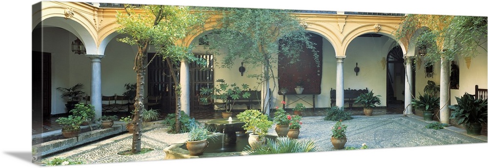 Long photo on canvas of a Spanish courtyard garden with a bunch of potted plants.