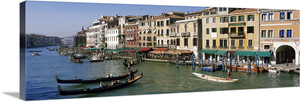 Large panoramic of a busy canal in Venice, Italy with gondola's and boats floating on the water and tourists walking along...