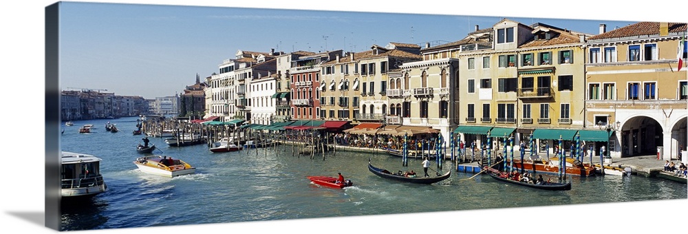 Buildings that line part of the Grand Canal are pictured in wide angle view with various types of boats gliding in the water.