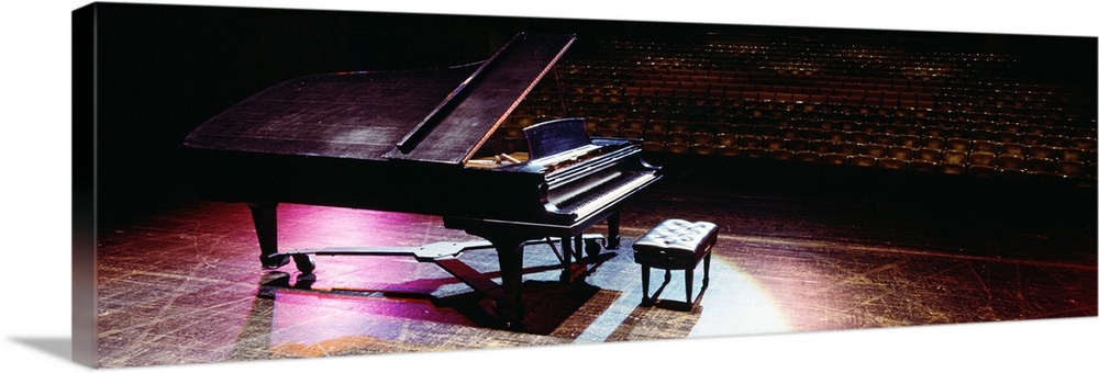 Full grand piano on a well-worn stage in a theater, looking out onto the rows of empty seats, under violet spotlights.