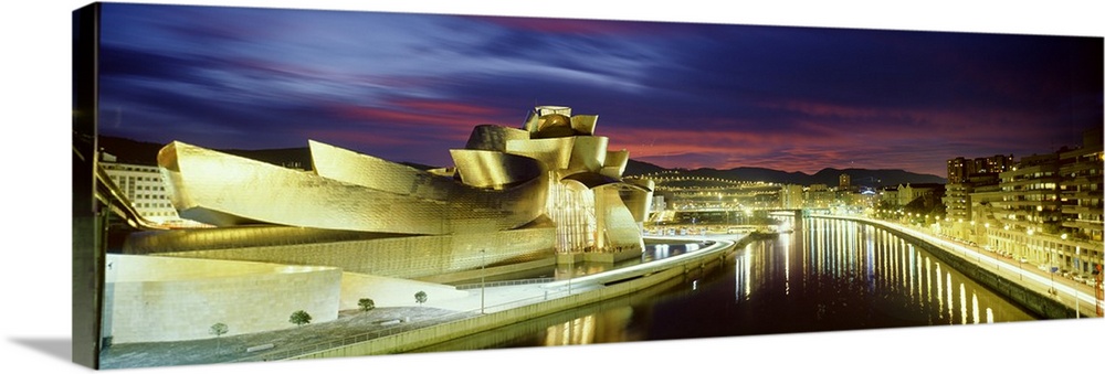 A beautifully architected museum in Spain is illuminated brightly under a sunset sky.