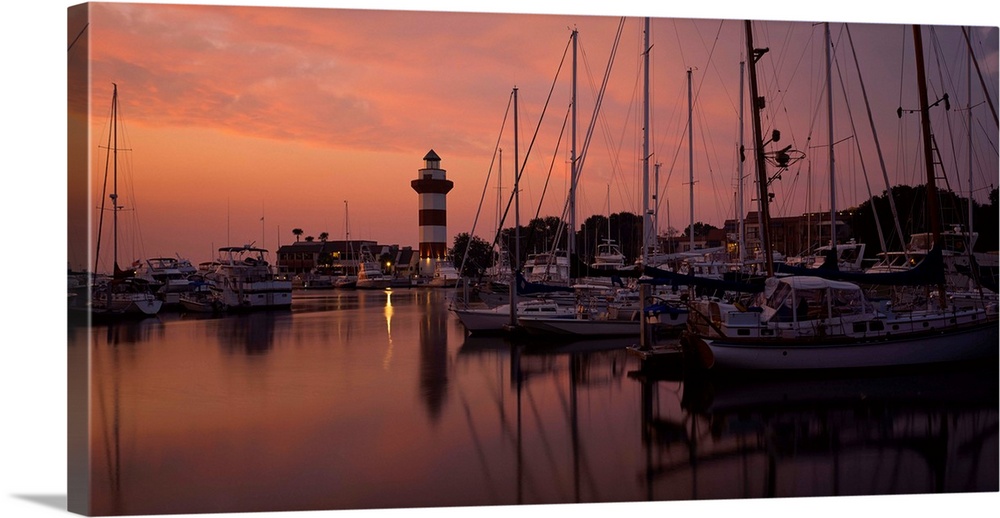 Big photograph displays a marina full of sailboats and other watercraft docked under the dimming light of the sky, while a...