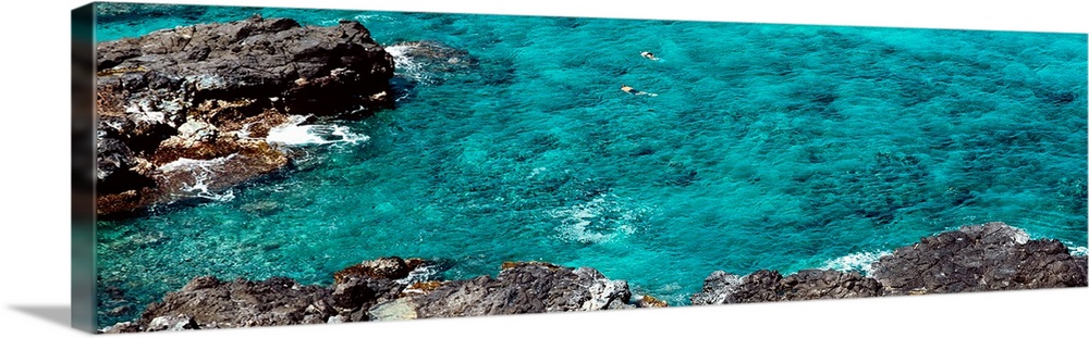 This panoramic photograph shows two figures from distance in clear waters of a reef.