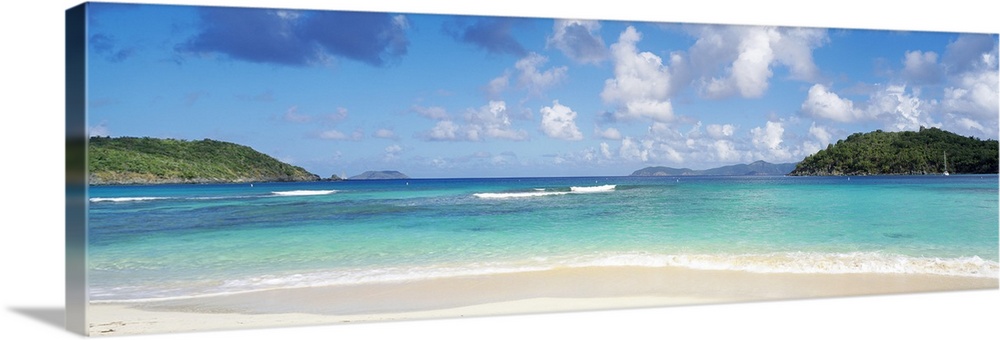 Panoramic photo of a white sand beach with crystal clear water and two land masses off in the distance on either side.