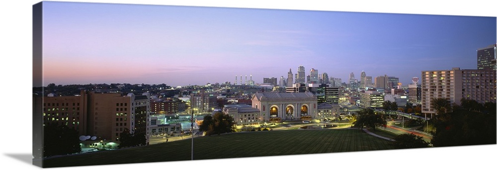 Wide angle photograph taken of the Kansas City skyline with the buildings illuminated under a dusk sky.