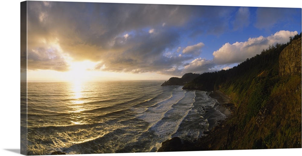 Photograph of steep shoreline with waves rolling in under a bright cloudy sky at sunrise.