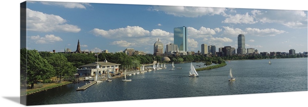 A panoramic photograph of Charles river with sail boats and the Boston skyline in the background. Trees line the edge of t...