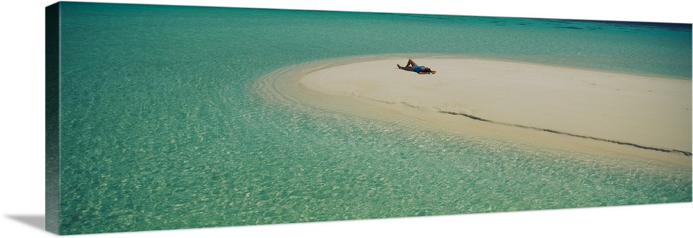 Panoramic photograph of girl tanning on sand bar surrounded by crystal clear ocean.