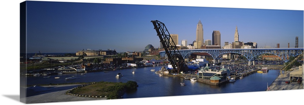 Panoramic photograph of bridge with port and sailboats below with skyline in the distance under a clear sky.