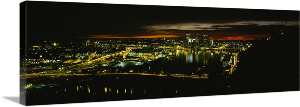 Wide angle, aerial photograph of the city of Pittsburgh, Pennsylvania, brightly lit at night.