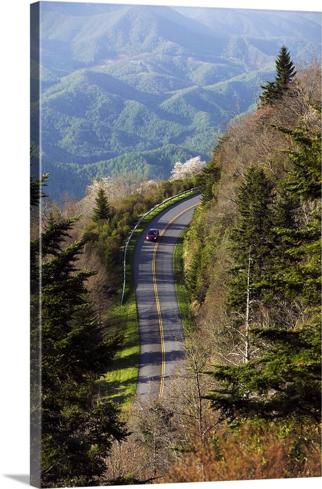 Tall photo on canvas of a car driving down a road on a mountainside with other mountains in the distance.
