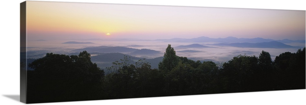 Large panoramic photograph of mountains in Virginia with the sun setting far in the distance and a layer of fog over the m...