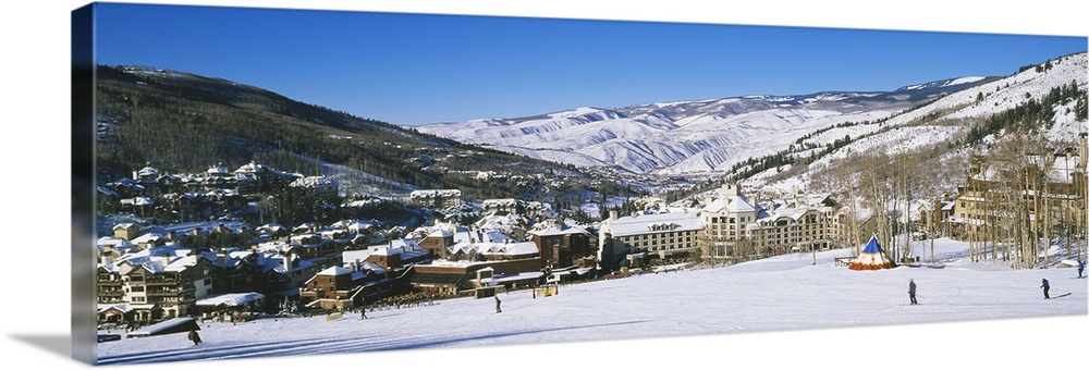 Panoramic photograph of ski lodge nestled in the valley of snow covered mountains under a clear sky.