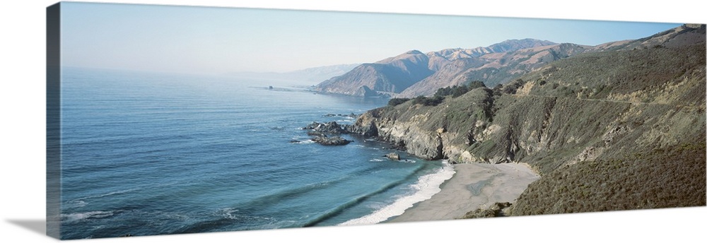 Panoramic image of the Pacific Ocean meeting rocky cliffs and a smooth beach.