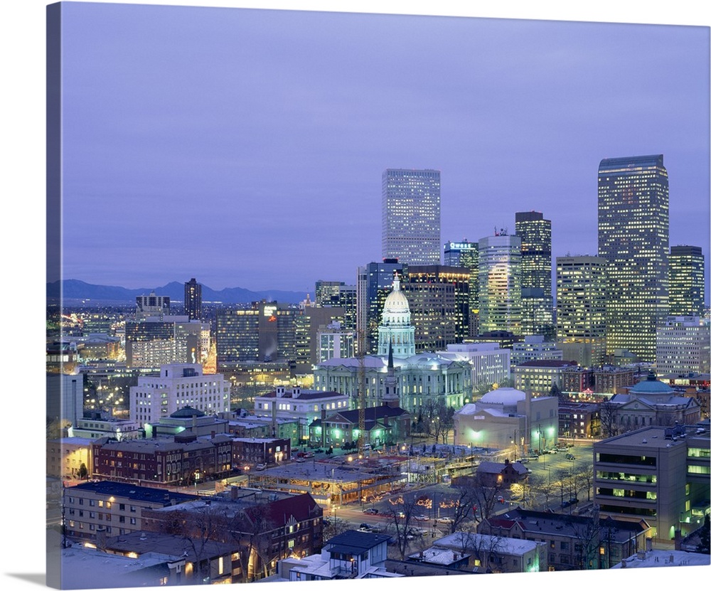 Square canvas photo of a illuminated city at dusk with mountains in the left background.