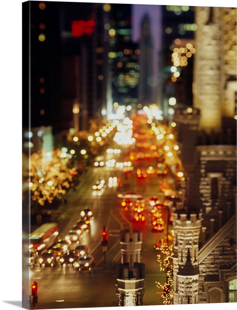 Vertical panoramic photograph of busy street lined with tall buildings that are lit up in the night sky.