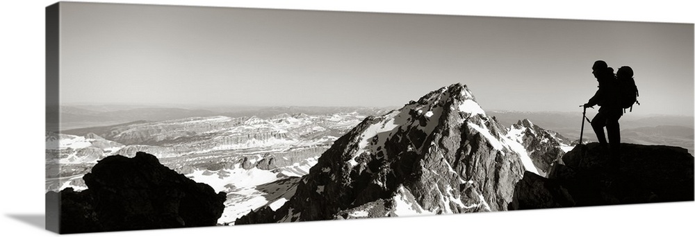 This panoramic photograph shows mountain peaks and the silhouette of a climber surveying the landscape.