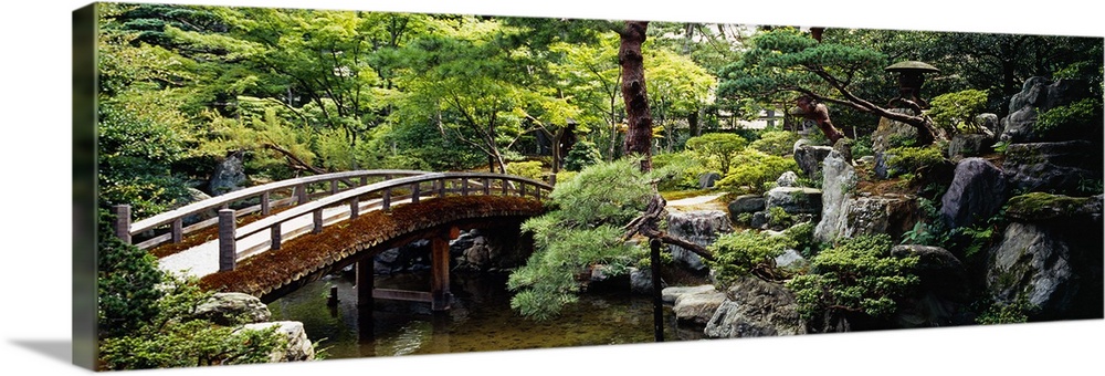 Panoramic photo on canvas of a bridge leading over a river with a garden on the right.