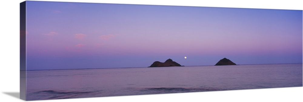 Giant horizontal photograph of a pastel sky over the water near Oahu, Hawaii, the Na Mokulua Islands on the horizon, at dusk.