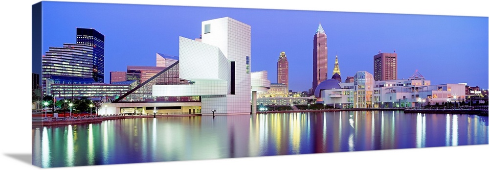 Large, panoramic photograph of the Cleveland skyline at dusk, reflecting in the waters of Lake Erie.